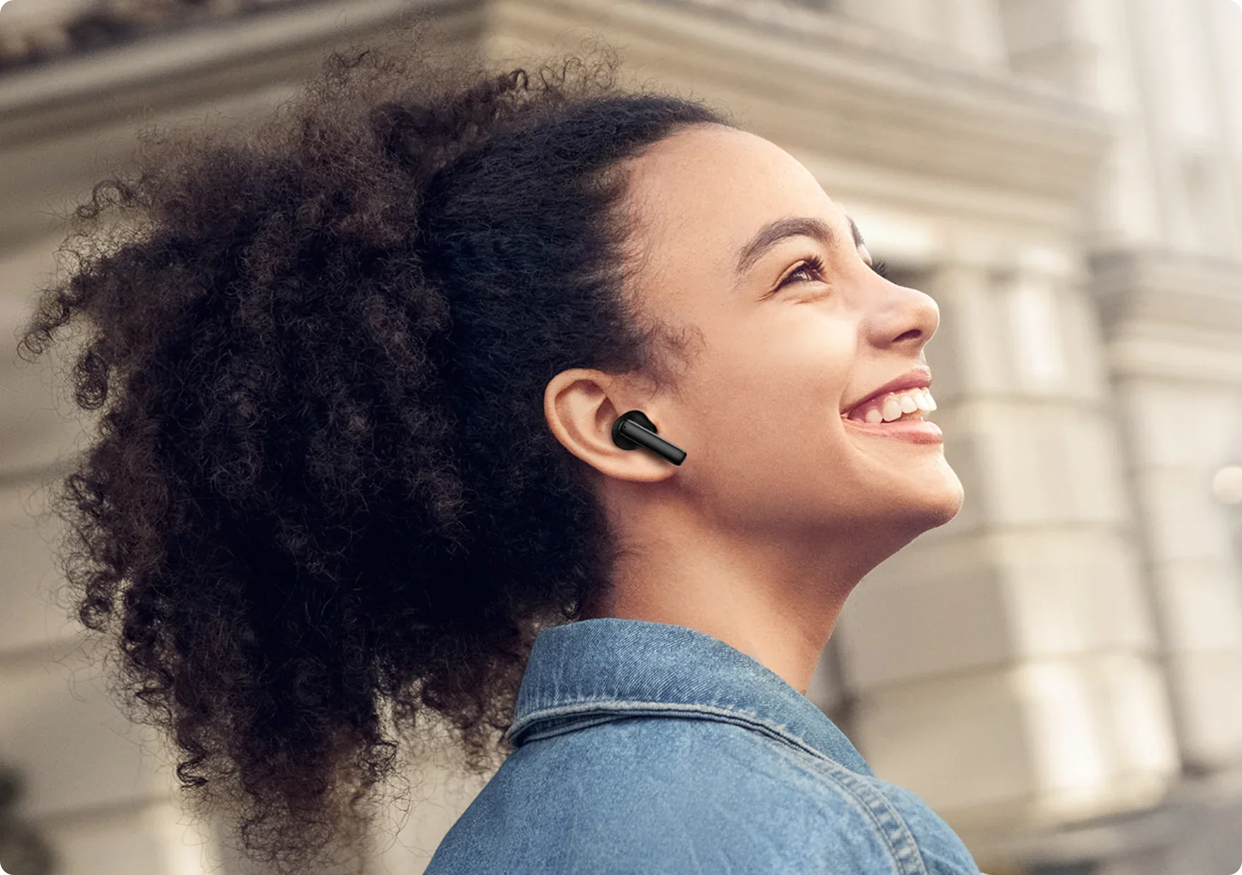 Mulher sorrindo com fone de ouvido sem fio preto, estilo casual ao ar livre.