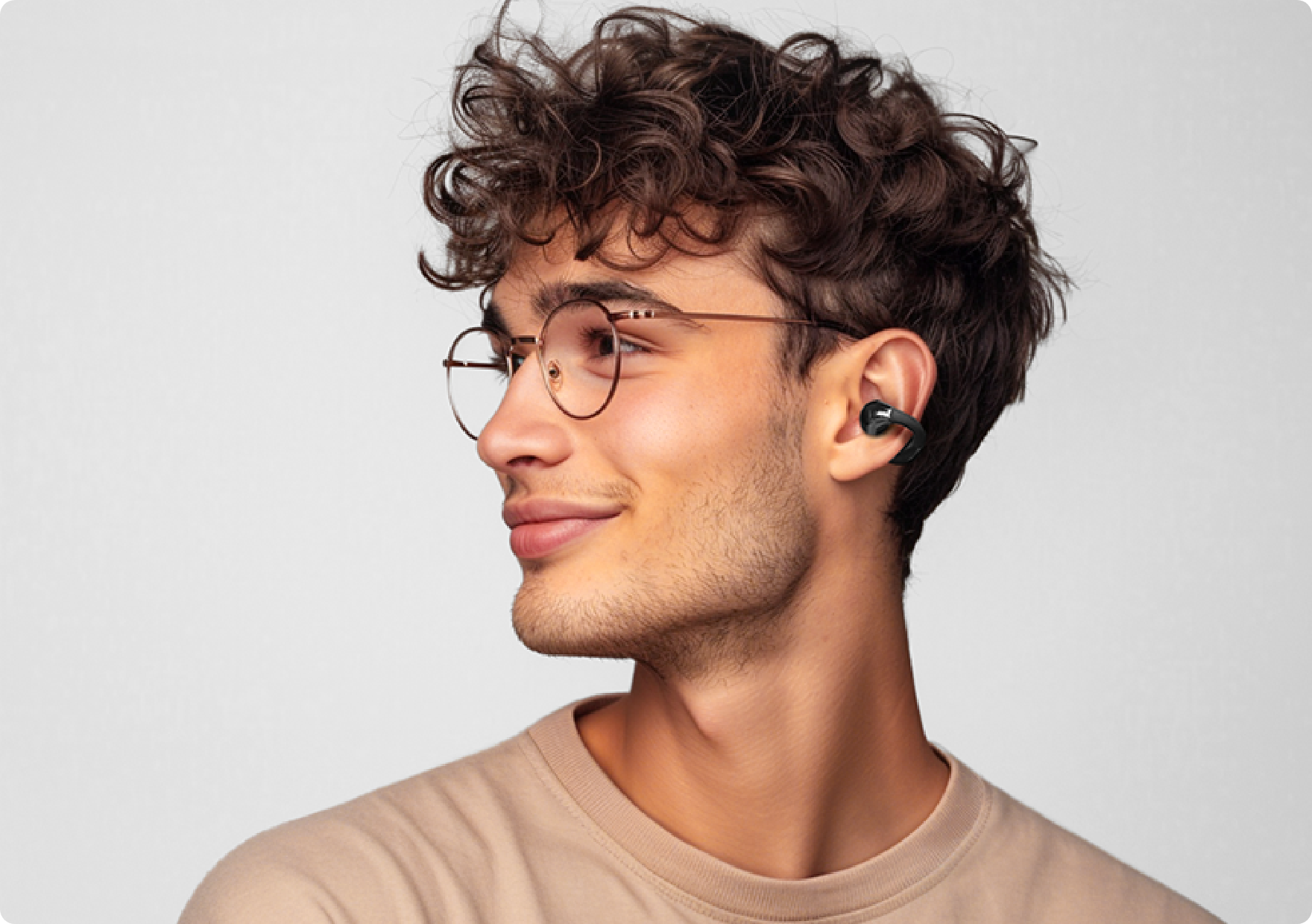 Homem com óculos usando fone de ouvido sem fio preto, perfil lateral, fundo claro.