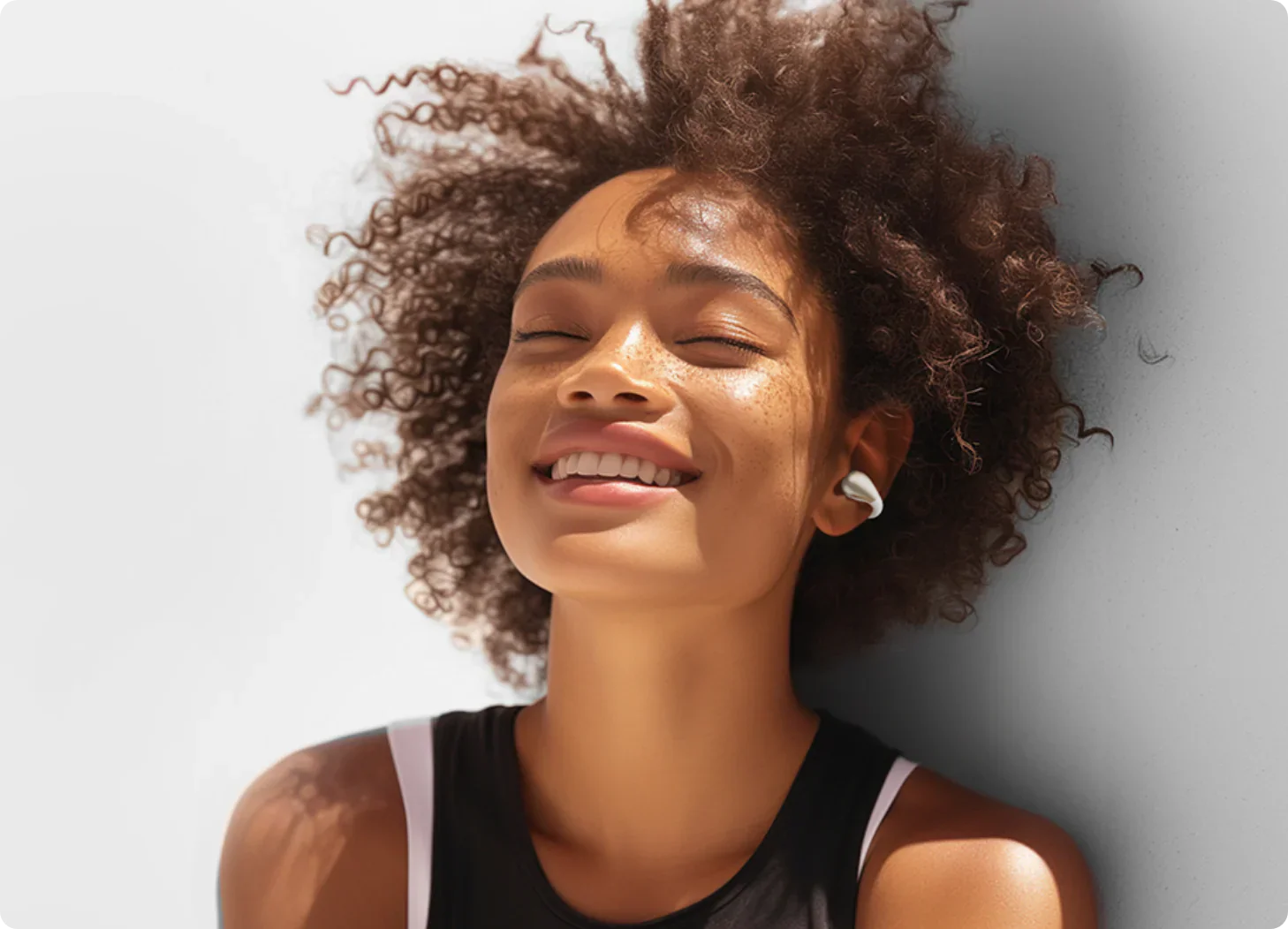 Mulher sorridente com fones de ouvido sem fio, aproveitando o sol. Estilo moderno e confortável para atividades ao ar livre.