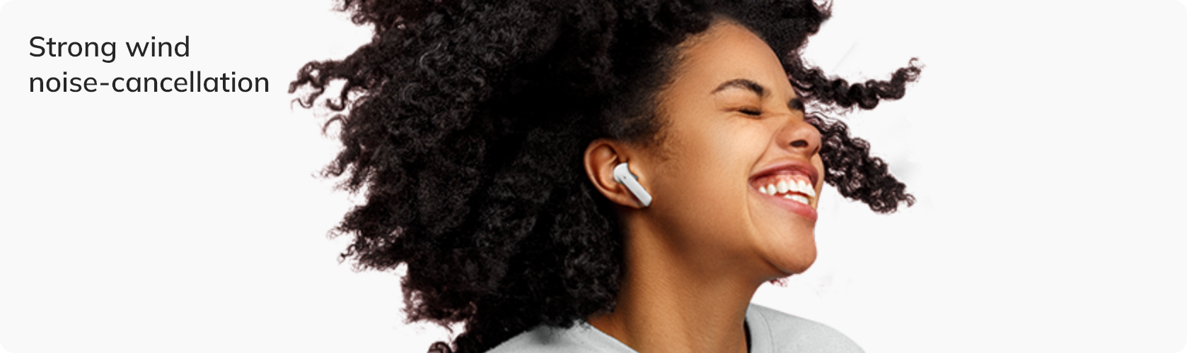 Mulher sorrindo com fones de ouvido sem fio, destacando cancelamento de ruído do vento.